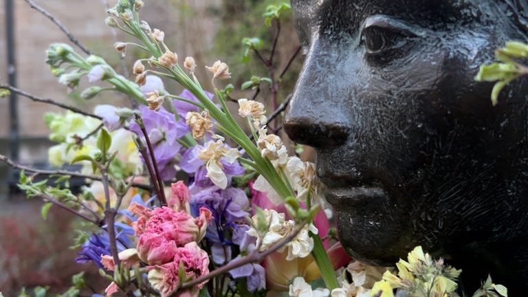 Man sieht den Kopf einer Statue. Links von ihr ist ein Blumenstrauß. Die Blumen sind schon leicht verwelkt. Bei der Statue handelt es sich um die "Sitzende" in Tübingen.  (Foto: SWR)