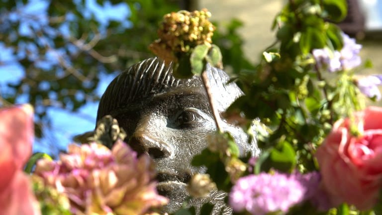 Man sieht den Kopf einer Skulptur. In Tübingen nennt man sie: die "Sitzende". Ihr werden oft Blumen in die Arme gelegt. Manchmal sieht man vor lauter Blümchen den Kopf gar nicht mehr.  (Foto: SWR)